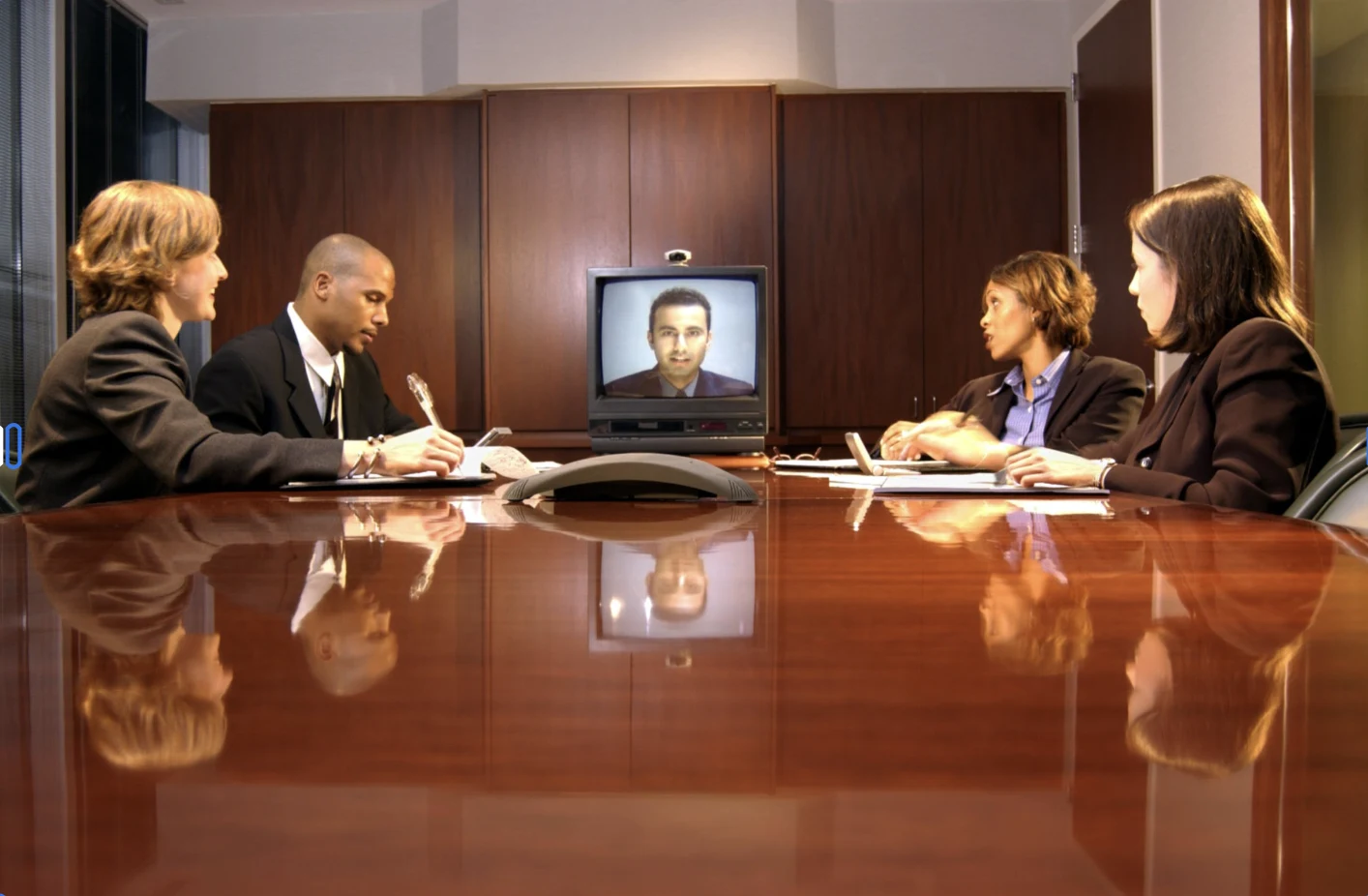A legal team meeting around a conference table with a remote participant on screen